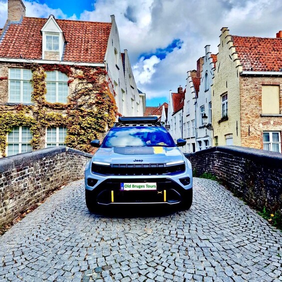 A white Jeep with a roof rack parked on a cobblestone street between buildings with red-tiled roofs and ivy-covered walls. 1