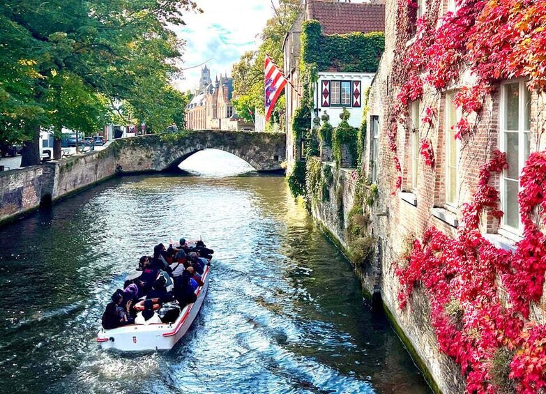 A narrow canal with a boat carrying passengers, a stone bridge, and buildings with ivy and flags. 4