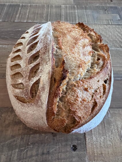 A loaf of artisan bread with a crusty exterior and a patterned cut on one side. 1