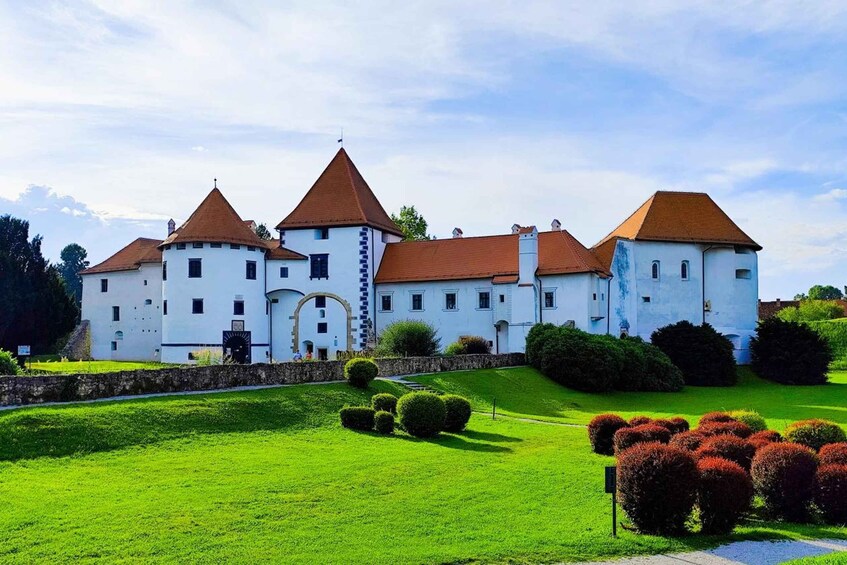 A castle with white walls and red roofs, surrounded by green lawns and bushes. 3