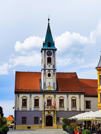 A historic building with a clock tower, flags, and a red-tiled roof. 2