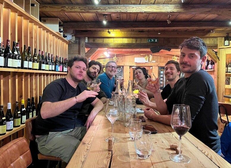 A group of people seated at a wooden table in a rustic bar setting with wine bottles on shelves behind them. 2