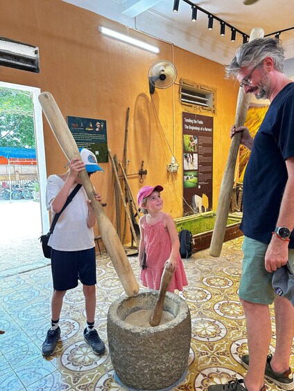 A museum exhibit with large stone tools, a child in a red dress, and adults observing. 5