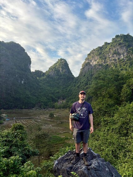 A person standing on a rock with a mountainous landscape in the background. 5