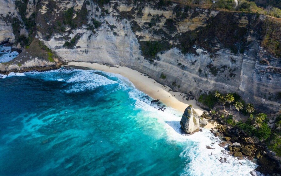 A coastal landscape with a sandy beach, clear turquoise waters, and a rocky cliff. 2