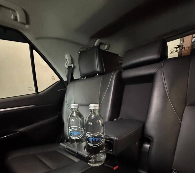 A car interior with black leather seats and two glass bottles labeled 'primo' on the center console. 5