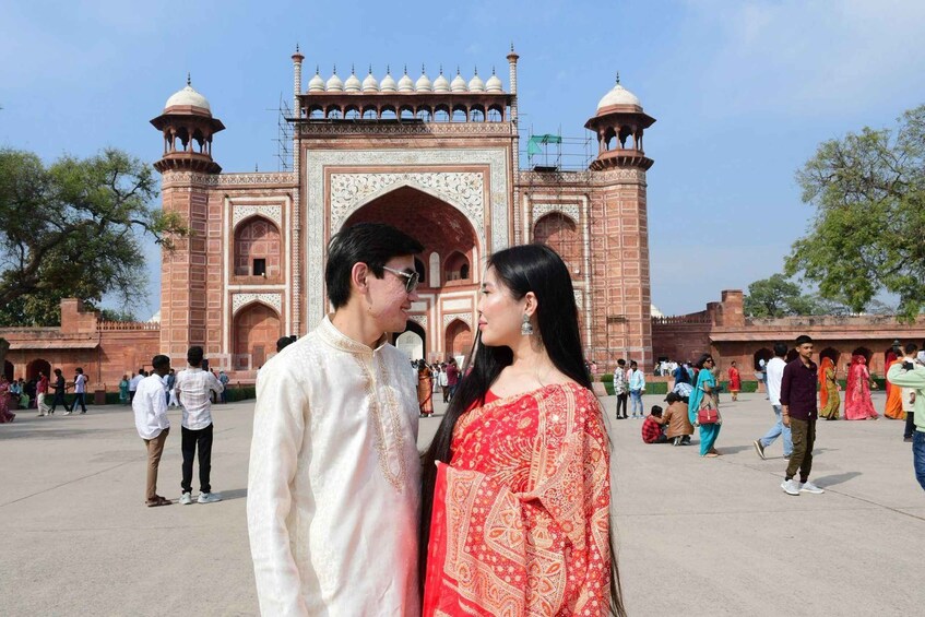 A couple in traditional attire standing in front of a historic red-brick gate with arches and domes. 5