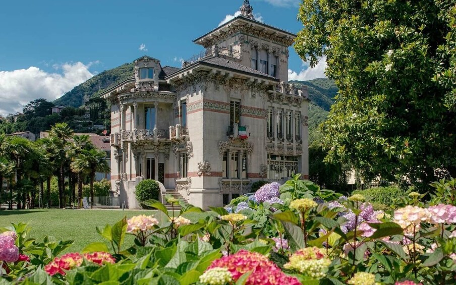 A historic building with ornate architecture, surrounded by lush gardens and mountains in the background. 1