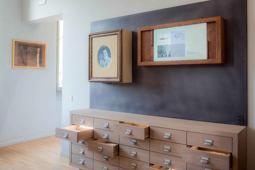 A gallery with framed artworks on the wall and a wooden cabinet with drawers. 4
