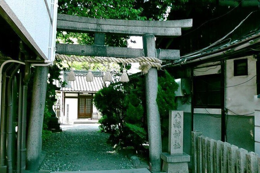 A traditional Japanese gate with a rope barrier, a stone lantern, and a building with a tiled roof in the background. 4