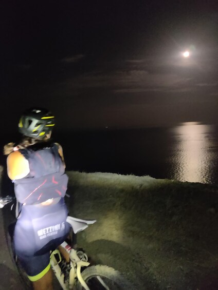 A person on a motorcycle at night by a body of water with a full moon in the sky. 3