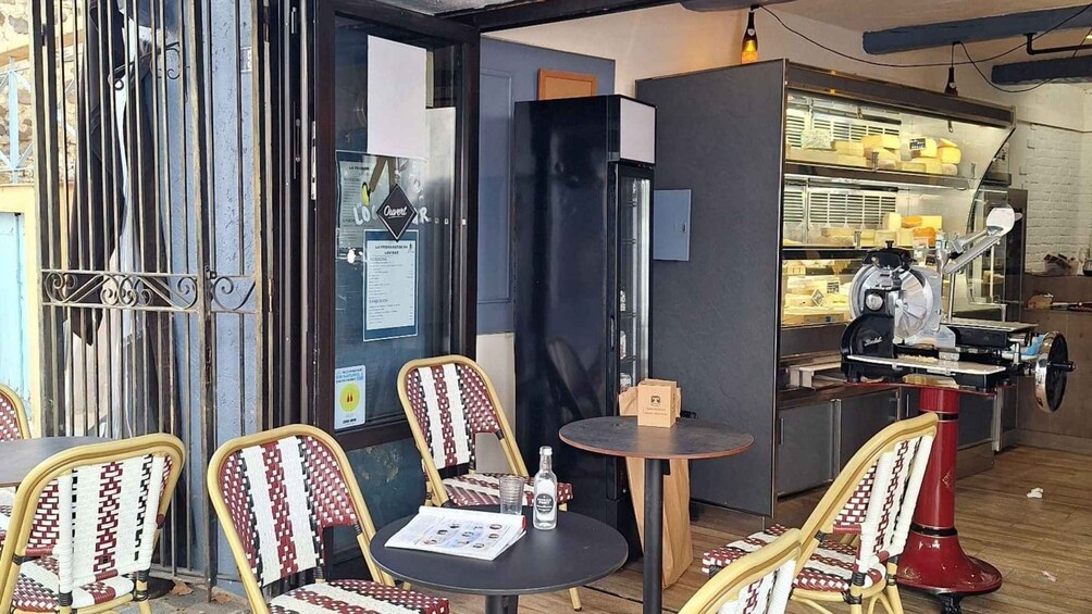 An outdoor café with wicker chairs and a small round table, a black refrigerator, and a food display case. 5