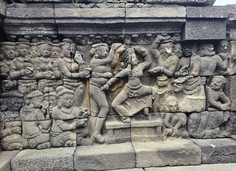 A stone relief with figures in various poses, some seated and others standing, with intricate carvings and a tiered structure above. 2