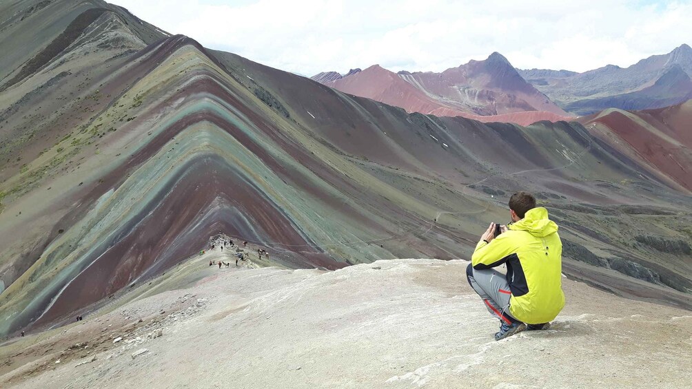 A person in a yellow jacket taking a photo of a colorful mountain landscape. 3