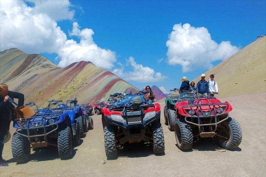 A group of ATVs parked on a dirt road with colorful mountains in the background. 2