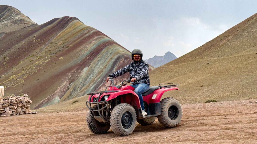 A person riding a red ATV in a mountainous area with colorful rock formations. 1