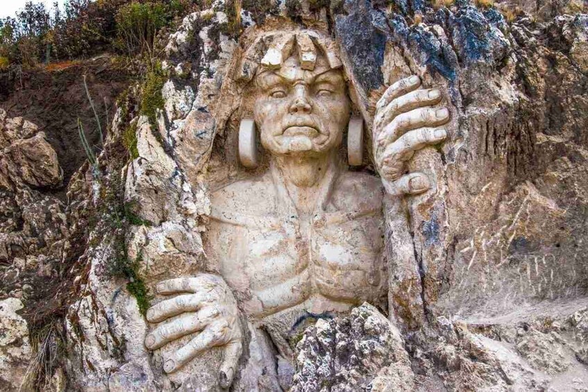 A rock carving of a human figure with hands raised, surrounded by natural rock formations. 4