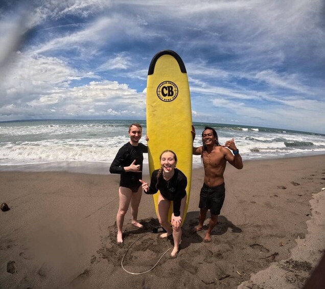 Three people on a beach holding a yellow surfboard with 'CB' logo. 3