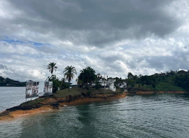 A coastal landscape with palm trees, a white building, and a billboard by the water. 3