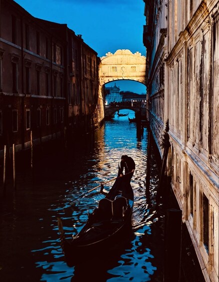 A narrow canal with a gondola and a bridge in the background. 1