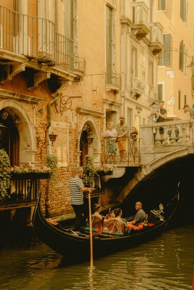 A gondola on a canal with passengers, a bridge, and buildings with balconies. 3