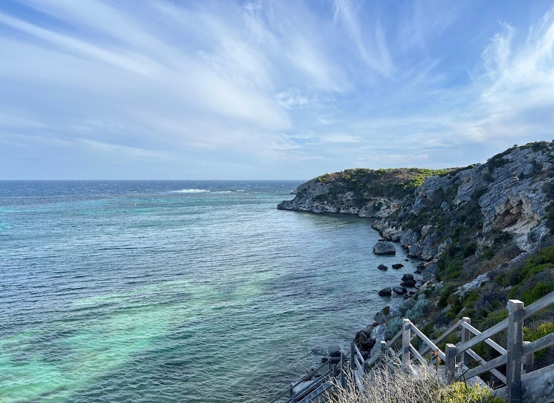 A coastal landscape with clear turquoise waters, rocky cliffs, and a wooden fence. 4