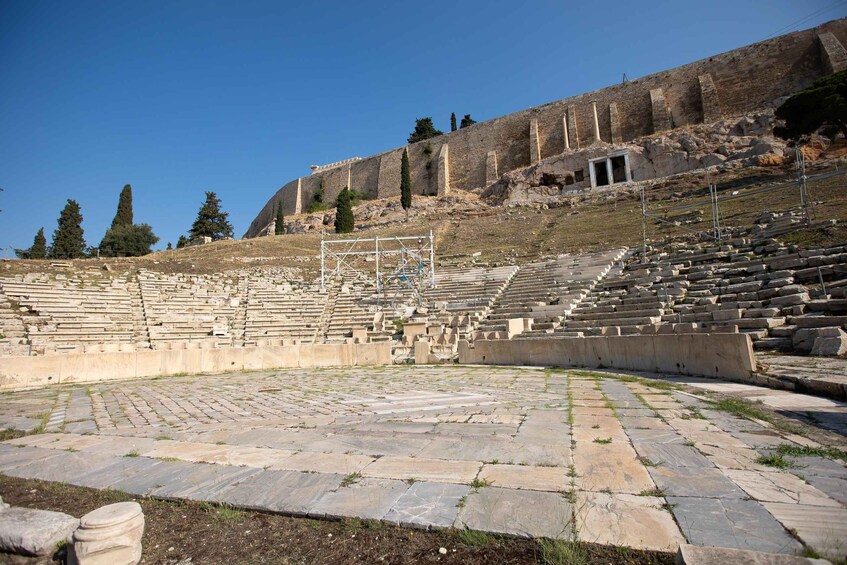An ancient amphitheater with stone seating and a stage, surrounded by a rocky hillside. 5