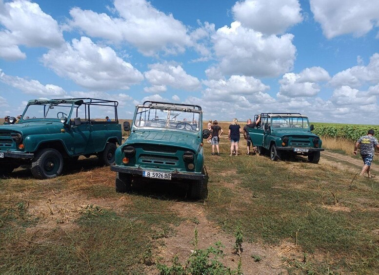 Three green off-road vehicles parked on a grassy field with people around them. 3