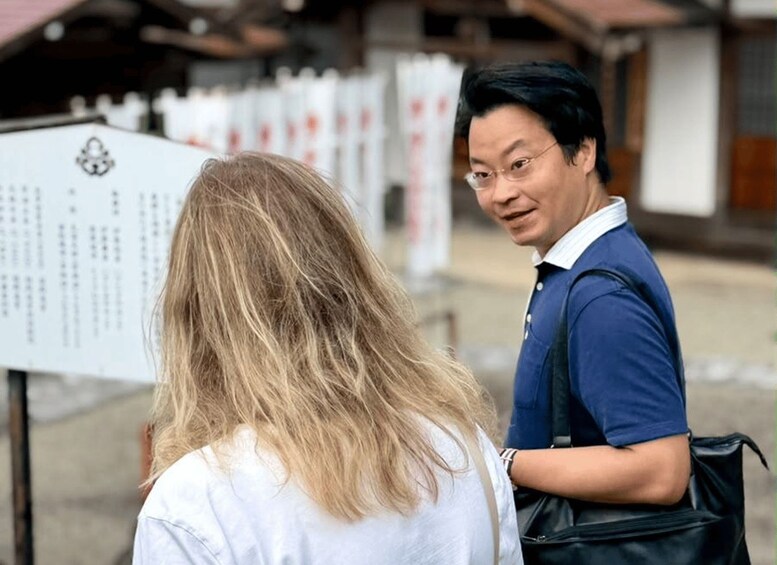 A person with blonde hair and a white shirt standing in front of a sign with text. 3