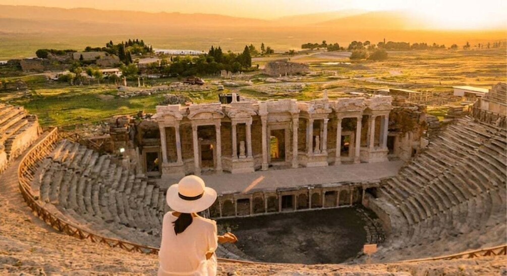 An ancient amphitheater with a central stage and audience seating, surrounded by ruins and greenery. 3