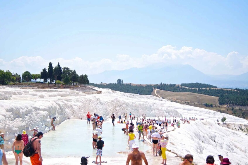 A group of people at a hot spring with white travertine terraces and mountains in the background. 2