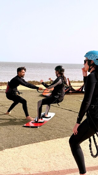 Three people engaged in a tug-of-war game on a sandy beach with the ocean in the background. 1