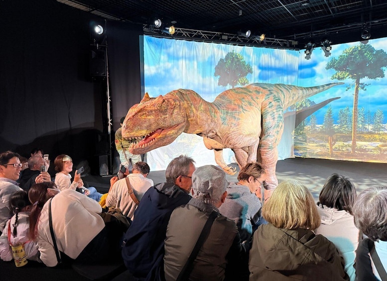 A large audience watching a presentation with a life-sized dinosaur model on stage. 5