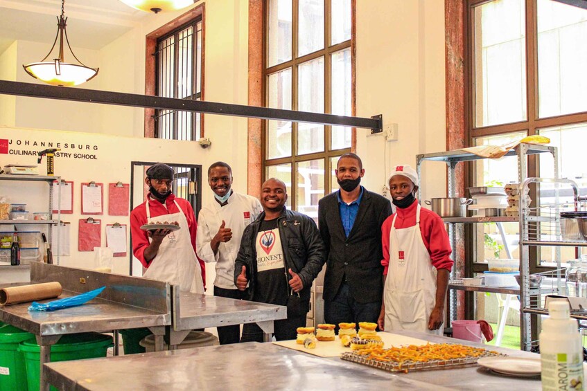 A group of people in a kitchen with a sign reading 'Johannesburg Culinary Arts School.' 5