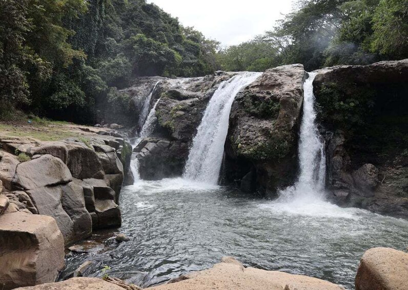 A waterfall cascading over rocks into a river, surrounded by dense forest. 2