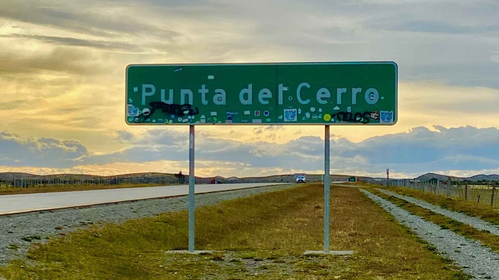A road sign with 'Punta del Cerro' written on it, set against a backdrop of a cloudy sky and a distant landscape. 3