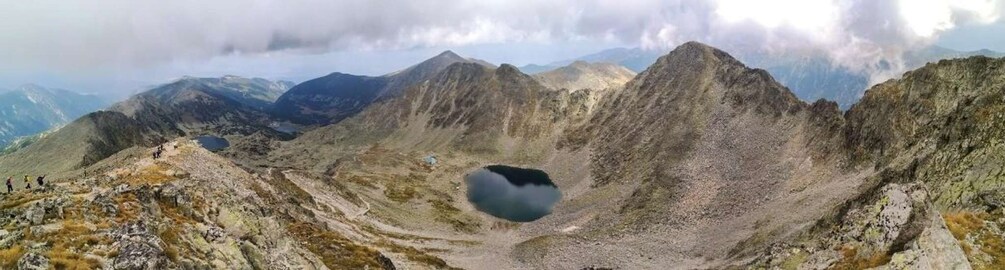 A mountainous landscape with a prominent lake and hikers in the distance. 1