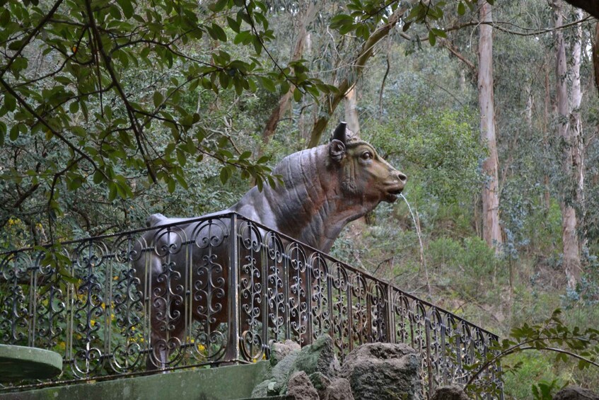 A large bronze elephant statue behind a wrought iron fence in a forested area. 2