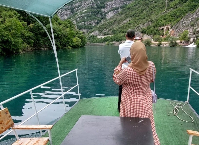 A boat with a covered deck, a table, and a railing. In the background, there is a body of water and a mountainous landscape. 4