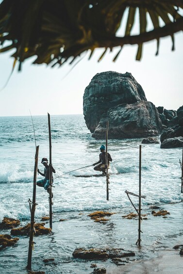 Two people fishing on a rocky beach with the ocean in the background. 1
