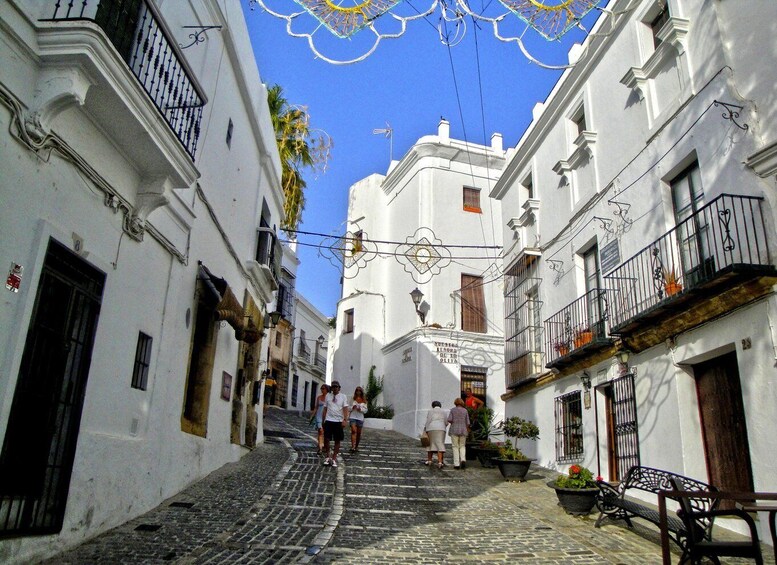 A cobblestone street flanked by white buildings with balconies, under a clear blue sky. 4