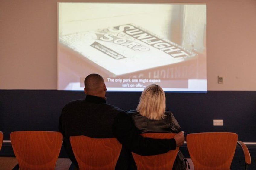 Two people seated facing a projection screen displaying a product. 2