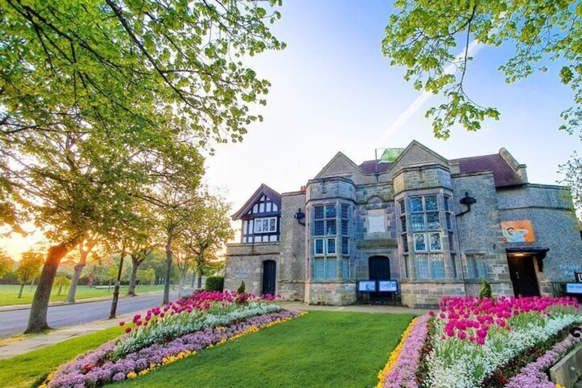A large stone building with a turret and a well-maintained garden with colorful flowers. 1