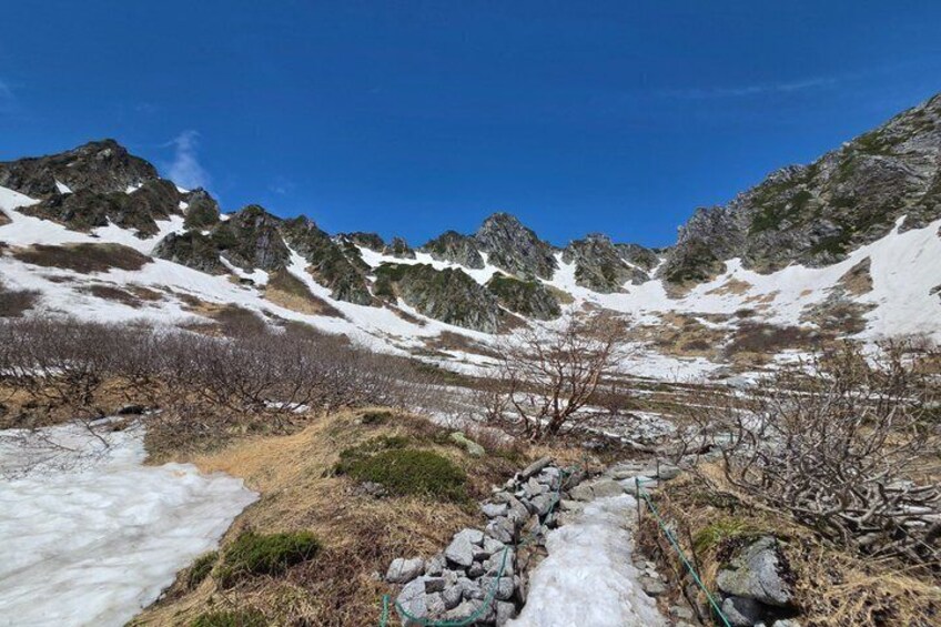 A snow-covered mountain path with rocky terrain and sparse vegetation. 5