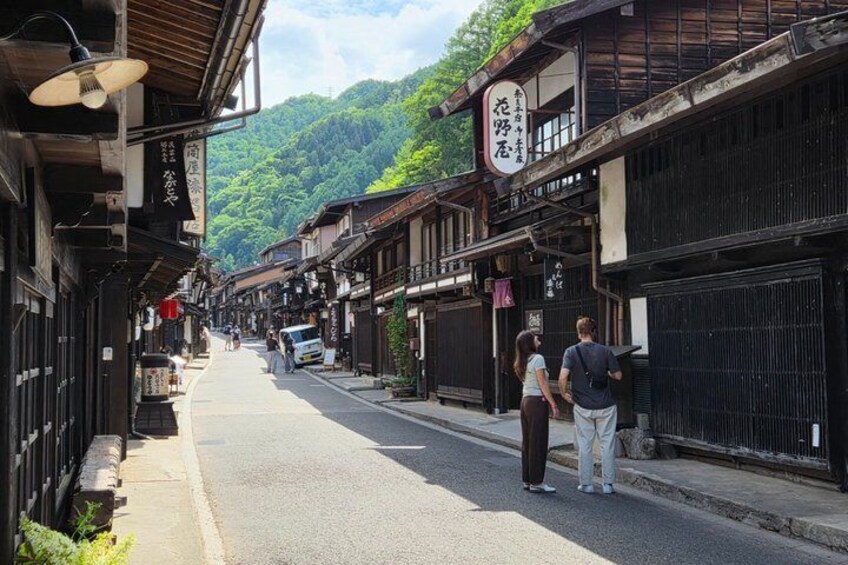 A narrow street lined with traditional buildings, a couple walking, and a sign with Japanese characters. 1