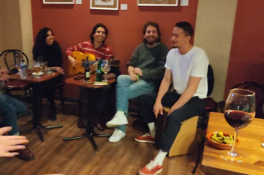 Un groupe de personnes est assis autour d’une table, avec des boissons et une guitare. 3