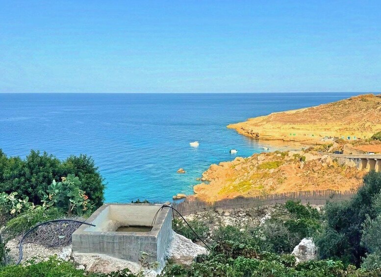 A coastal landscape with a clear blue sea, rocky terrain, and a concrete structure in the foreground. 3