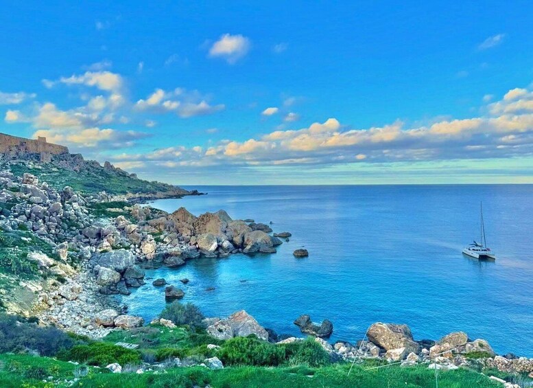 A coastal landscape with rocky terrain, a sailboat on the water, and a distant hill. 5