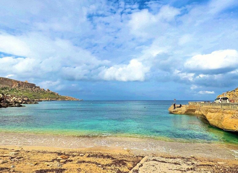 A coastal landscape with clear turquoise waters, rocky shorelines, and a distant cliff. 4