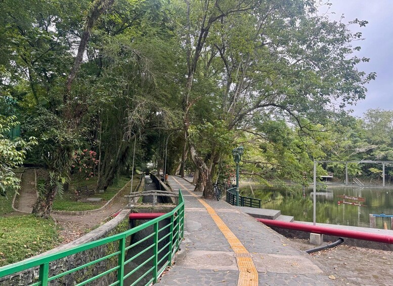 A pathway alongside a body of water, bordered by lush greenery and a stone railing. 2